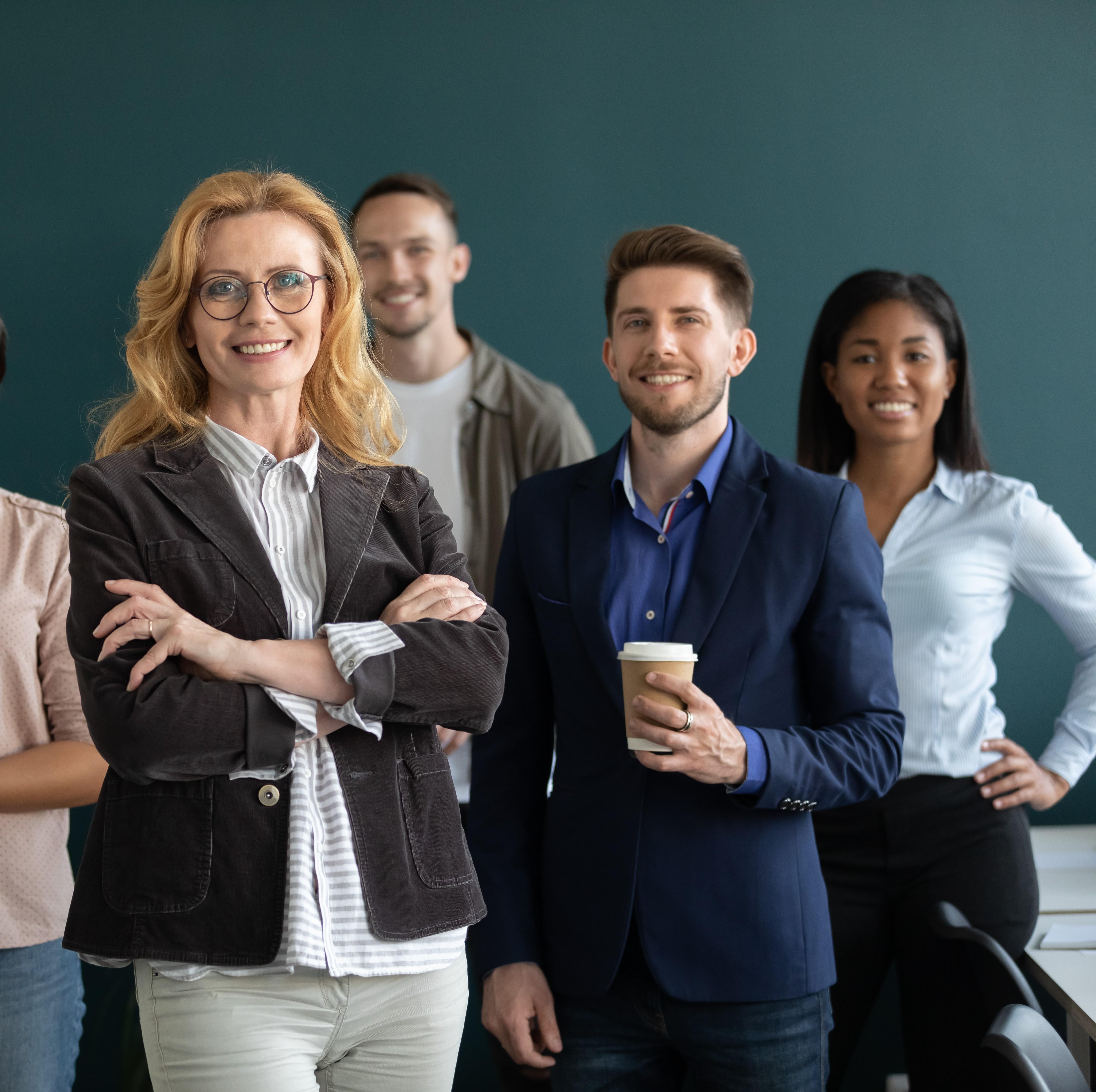 coworker with arms crossed smiling with coworkers behind holding coffee